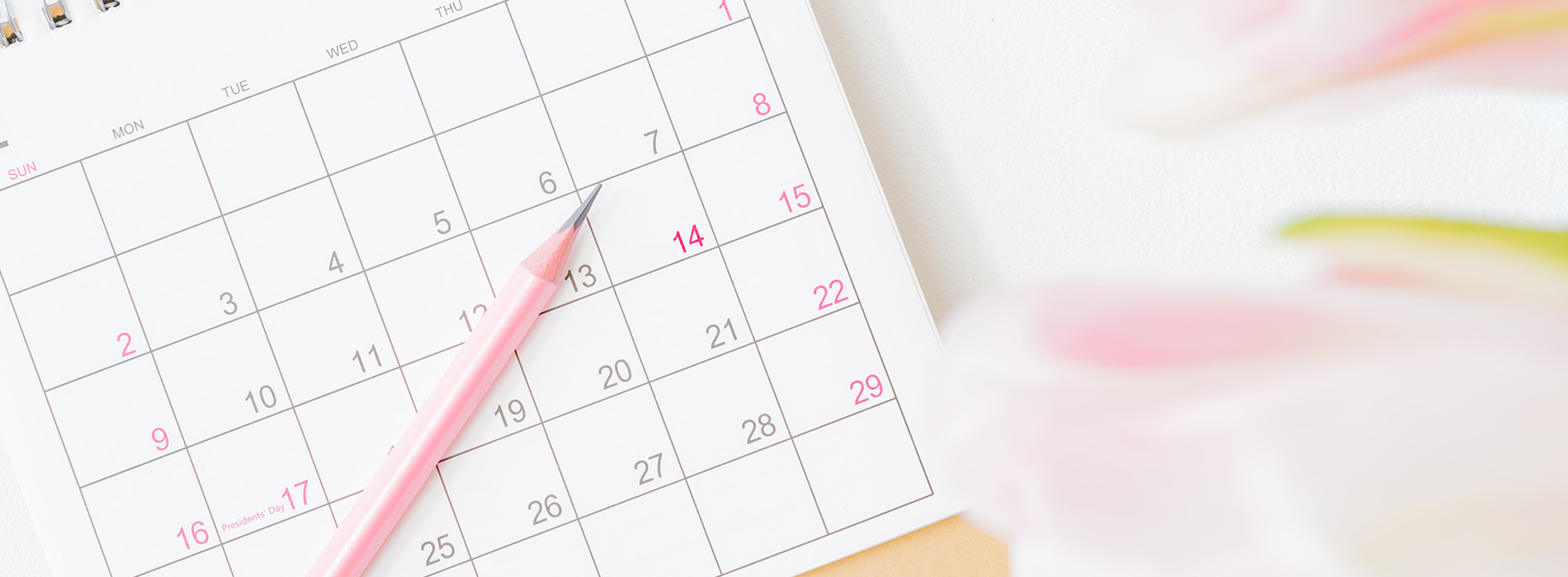 A pink pen on top of a paper calendar with the month of May visible, placed against a blurred background.