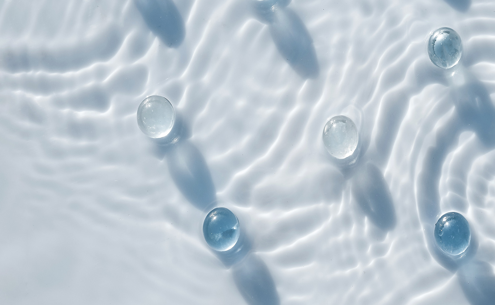 The image features a close-up of clear water droplets on a textured surface, with a blurred background that suggests a shallow depth of field.